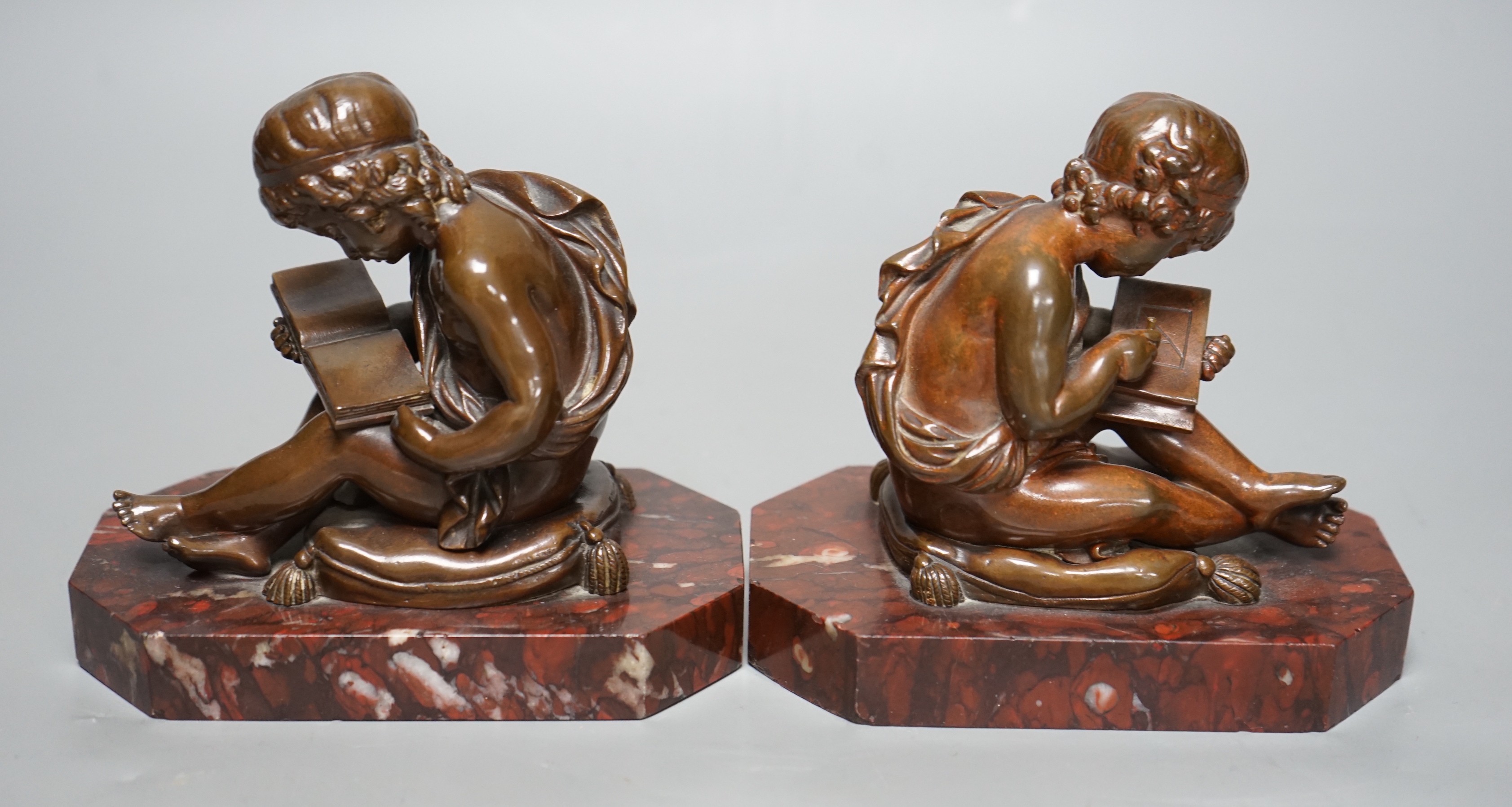After Charles Gabriel Lemire (1741-1827), a pair of bronze studies of boys seated on cushions, writing and reading, E. Colin & Cie, Paris foundry marks, on rouge marble bases, 14cm long